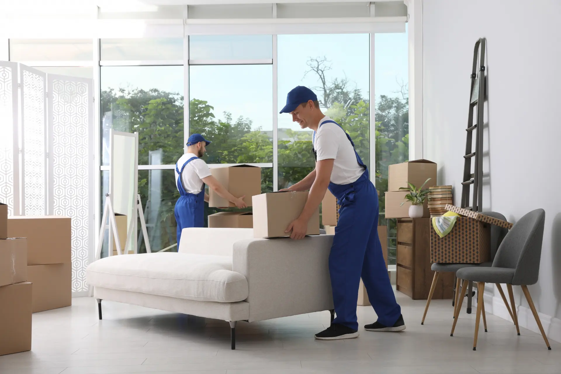 Two movers carrying a couch in a bright living room.