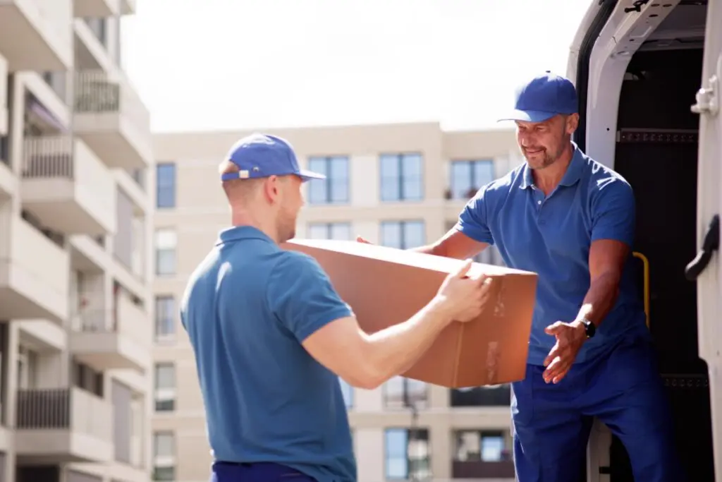 Two delivery workers handing over a large cardboard box outdoors.