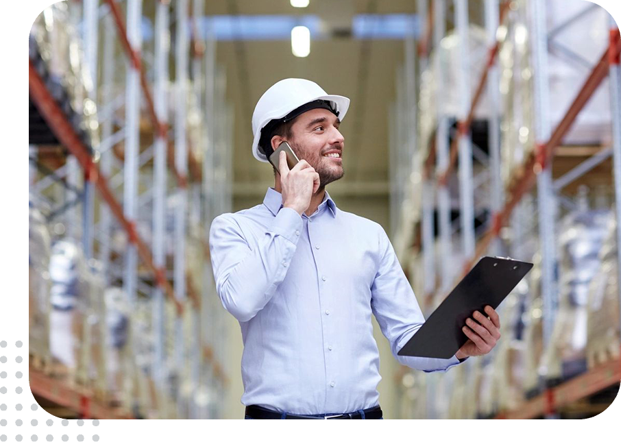 Warehouse worker wearing a helmet using a phone and clipboard.