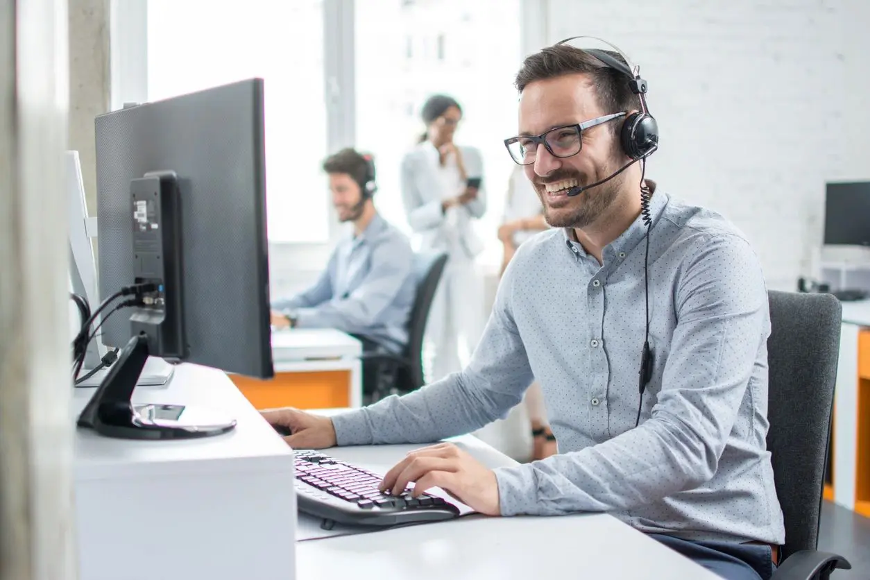 Smiling man wearing headset working at computer in office.