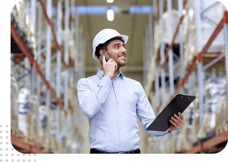 Warehouse worker wearing a helmet using a phone and clipboard.