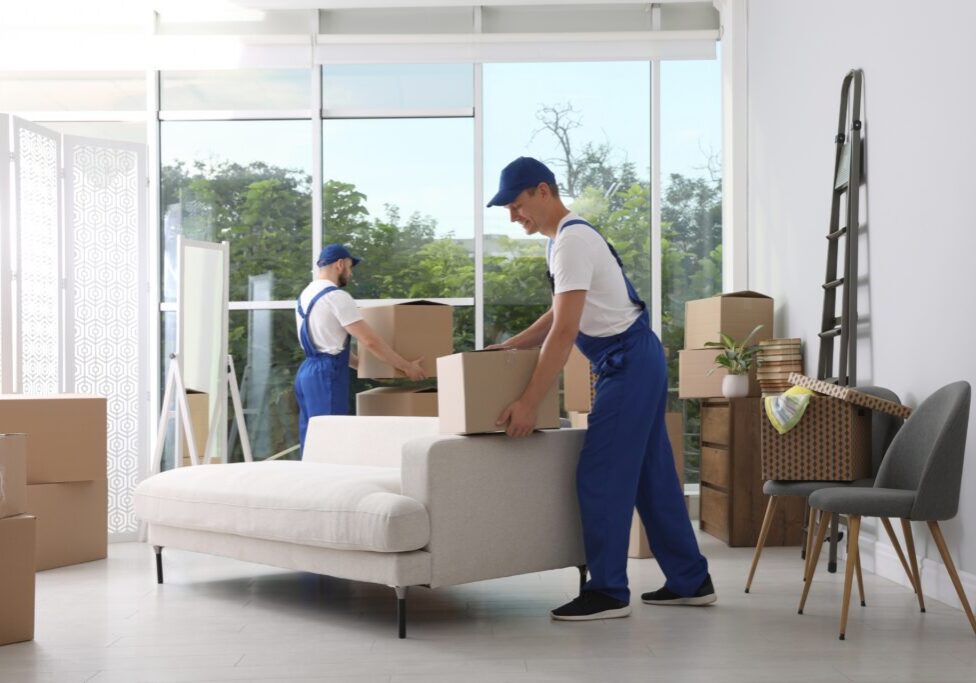 Two movers carrying a couch in a bright living room.